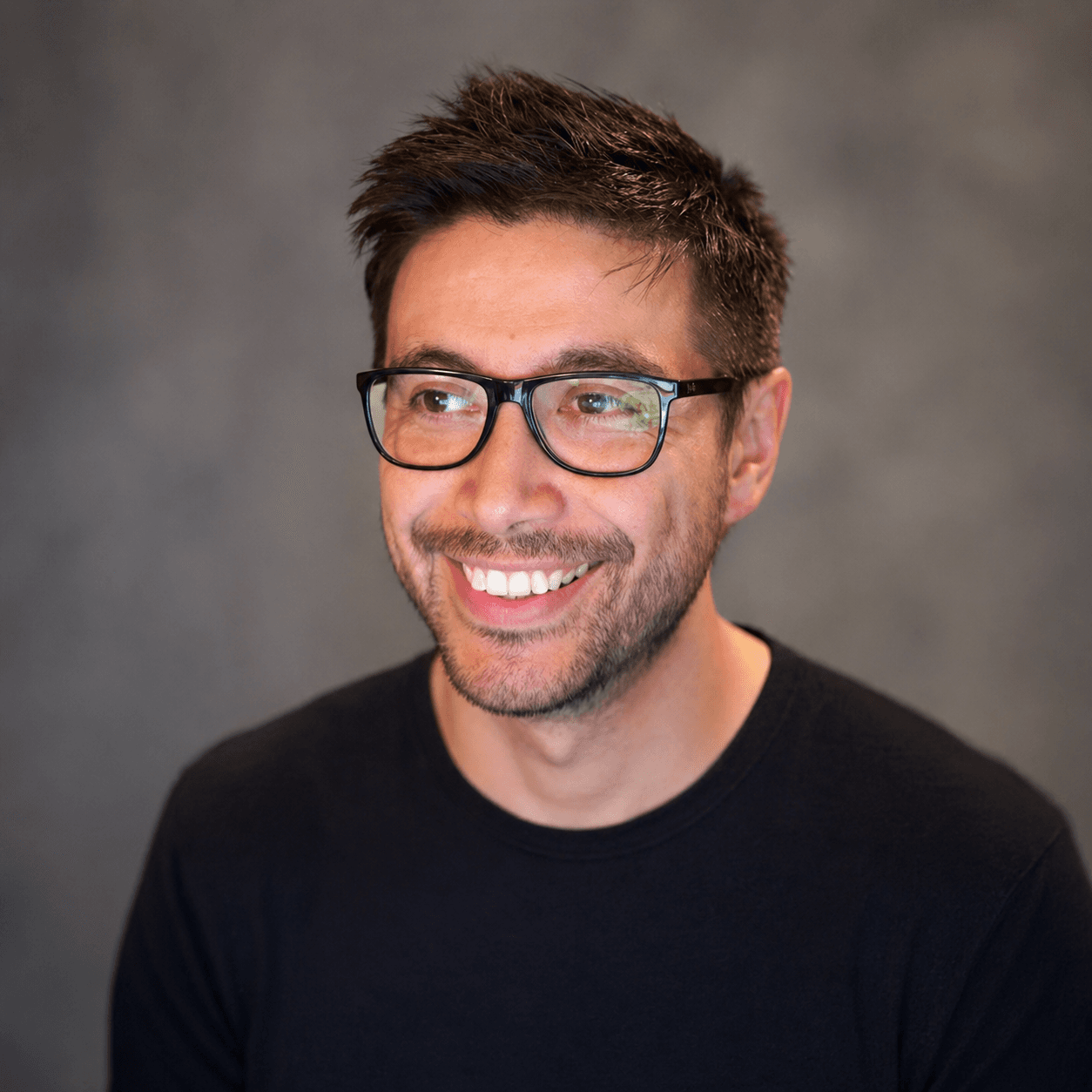 Jonathan Tipper smiling in a dark top and glasses